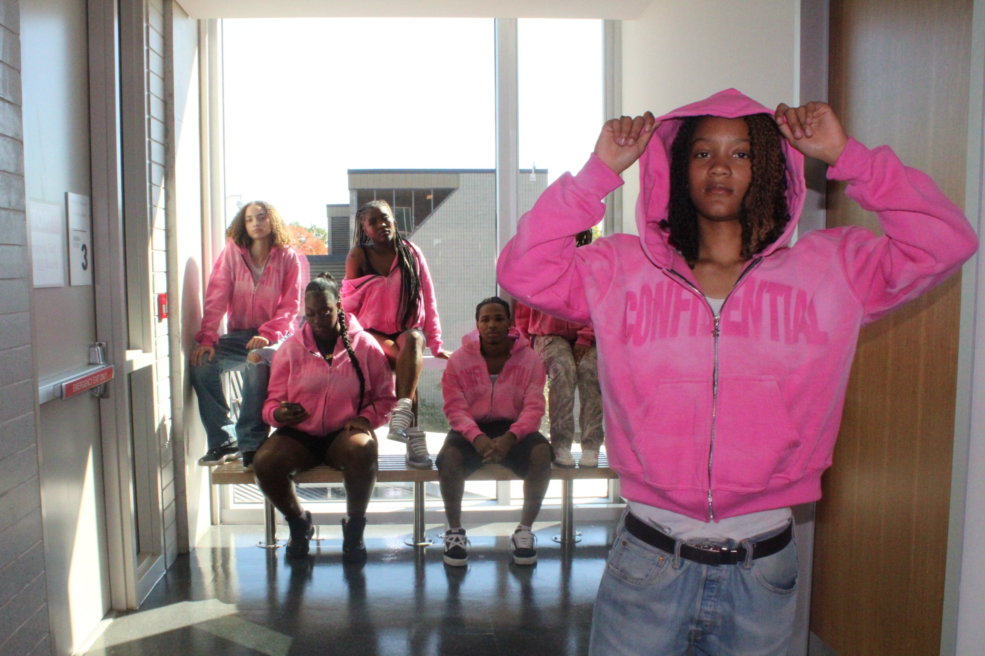 Person wearing a pink hoodie with 'CONFIDENTIAL' text in a hallway.